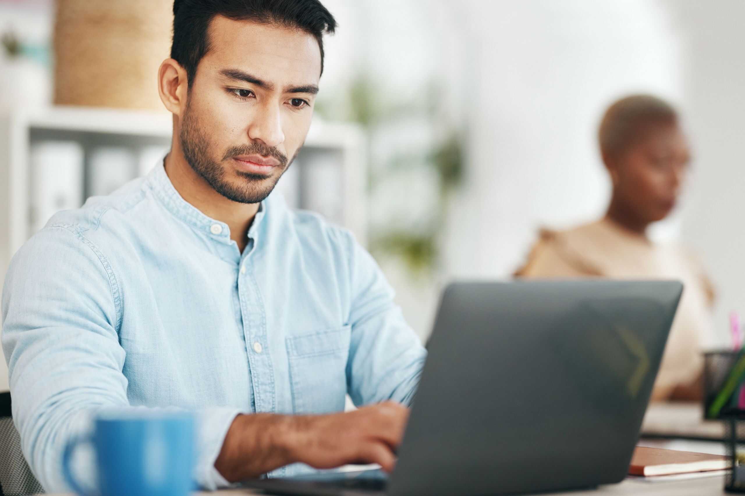 Young man studying on a laptop in a modern office setting, representing future IT education trends in New Zealand.